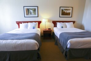 A hotel room with two single beds, a nightstand with a lamp, and framed pictures on the wall. - Lakeview Inns & Suites - Fort Nelson (Fort Nelson)
