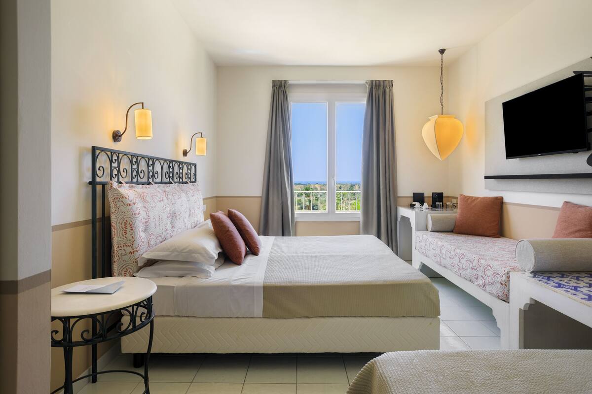 Une chambre d’hôtel avec un lit, un canapé, une télévision et un balcon avec des rideaux.