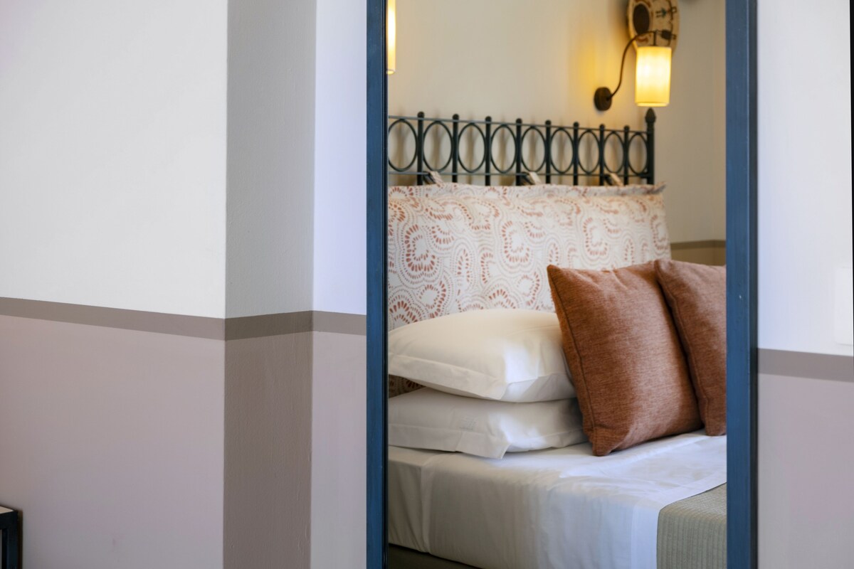 A neatly made bed with white and brown pillows, a patterned headboard, and a wall-mounted light fixture.