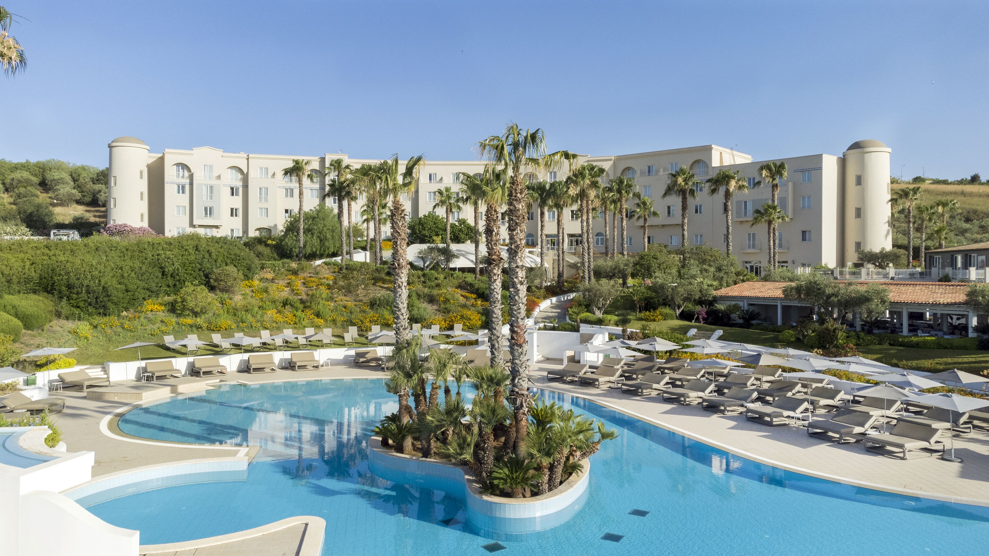A resort with a large pool surrounded by palm trees and lounge chairs.