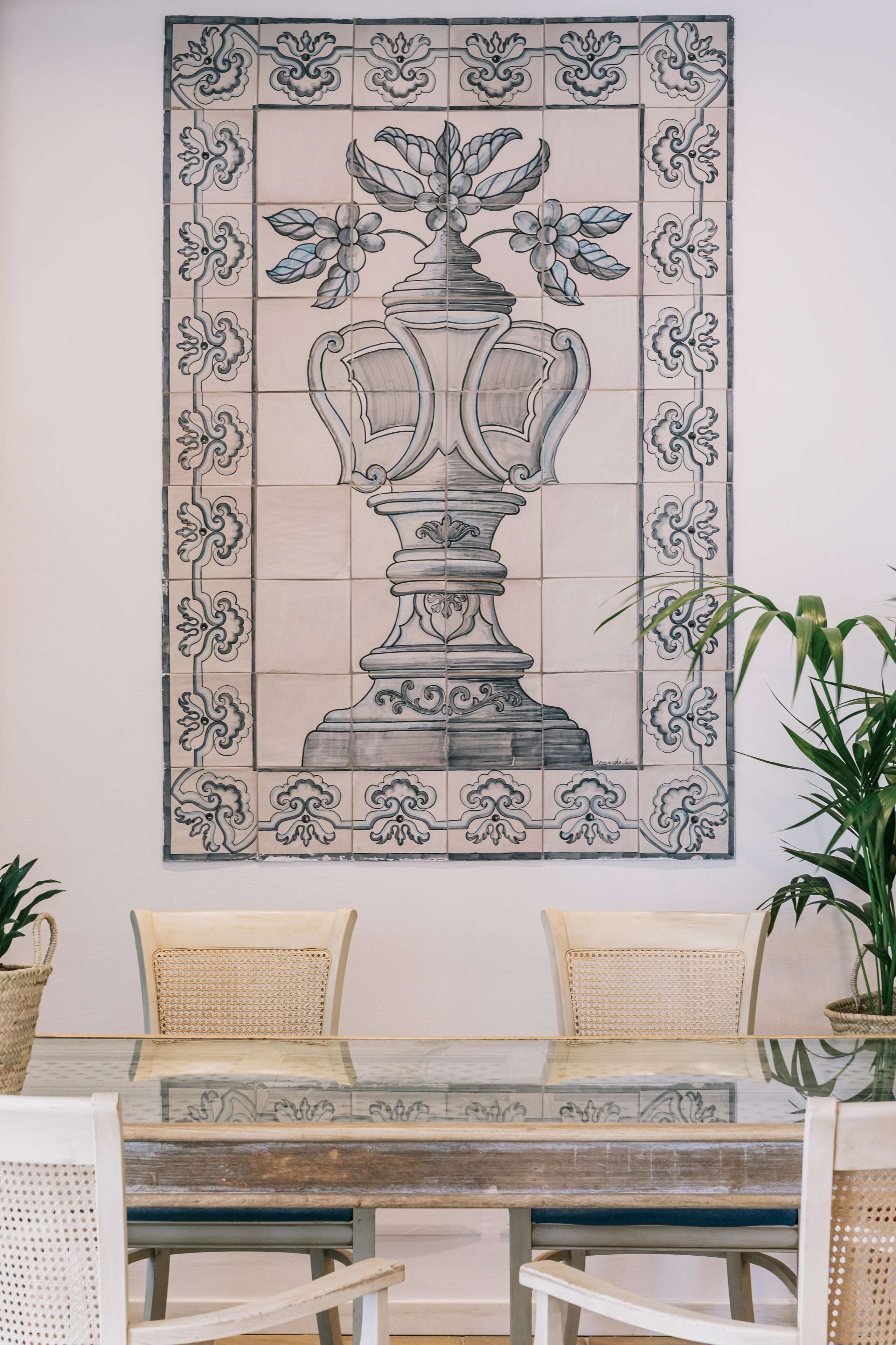 A dining area with a table set for two, surrounded by wicker chairs, and a decorative tile mural on the wall.