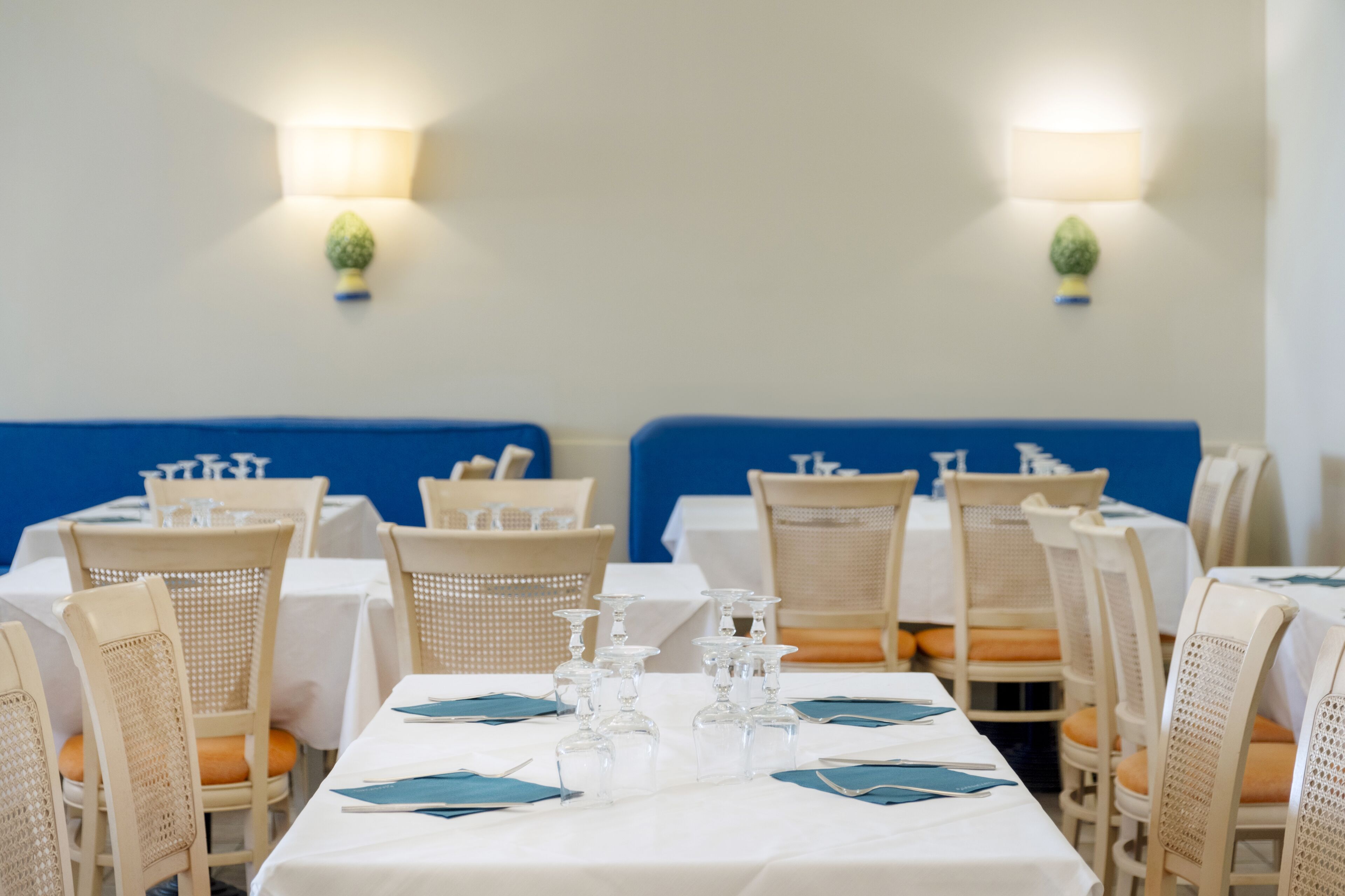 A dining area with white tables, wicker chairs, and blue cushions.