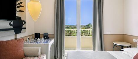 A hotel room with a bed, a sofa, a table with a vase, and a view of the outdoors.