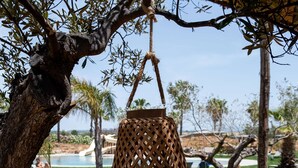 A hanging wicker lamp on a wooden deck with a pool and palm trees in the background. - Mangia's Selinunte Resort (Castelvetrano)