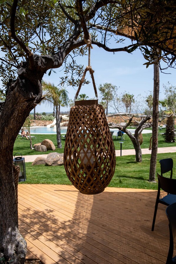 A hanging wicker lamp on a wooden deck with a pool and palm trees in the background. - Mangia's Selinunte Resort (Castelvetrano)