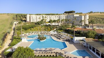Um resort com uma piscina grande, várias áreas de estar e um edifício em estilo arquitetônico mediterrâneo.