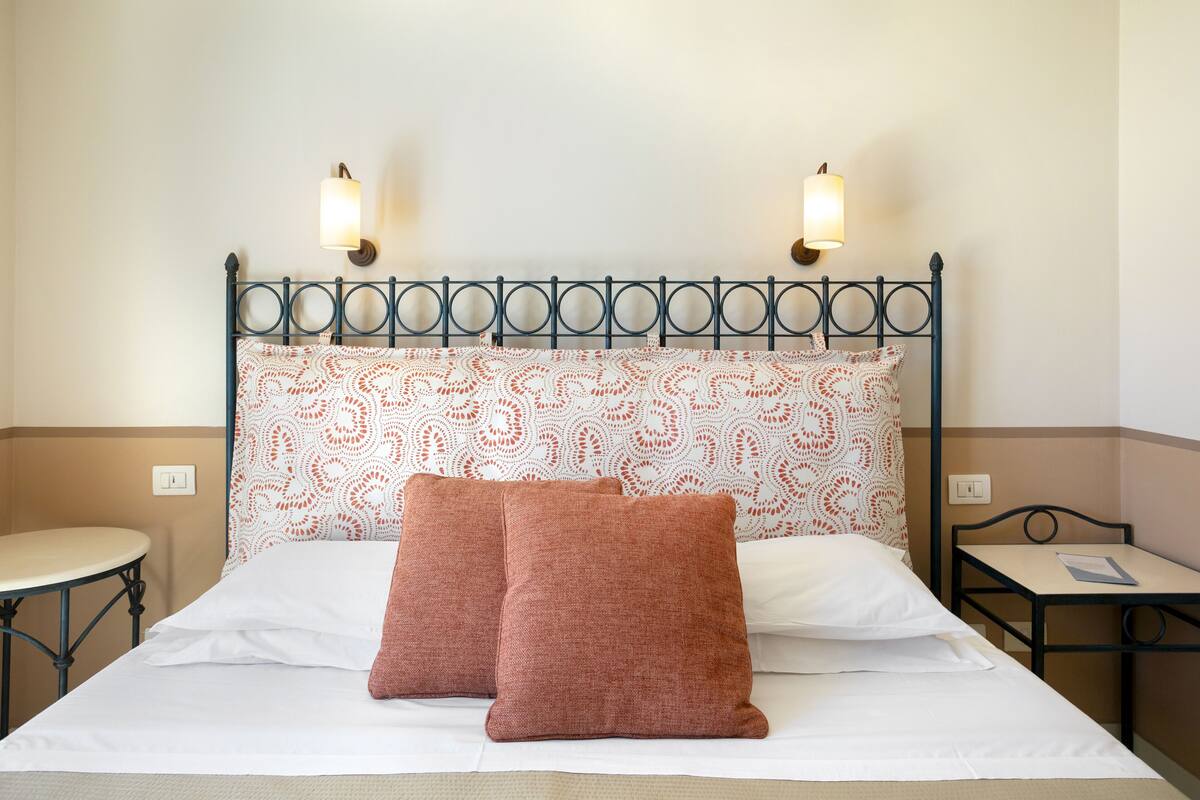 Un lit bien fait, avec une tête de lit décorée, deux tables de chevet et des lampes fixées au mur.