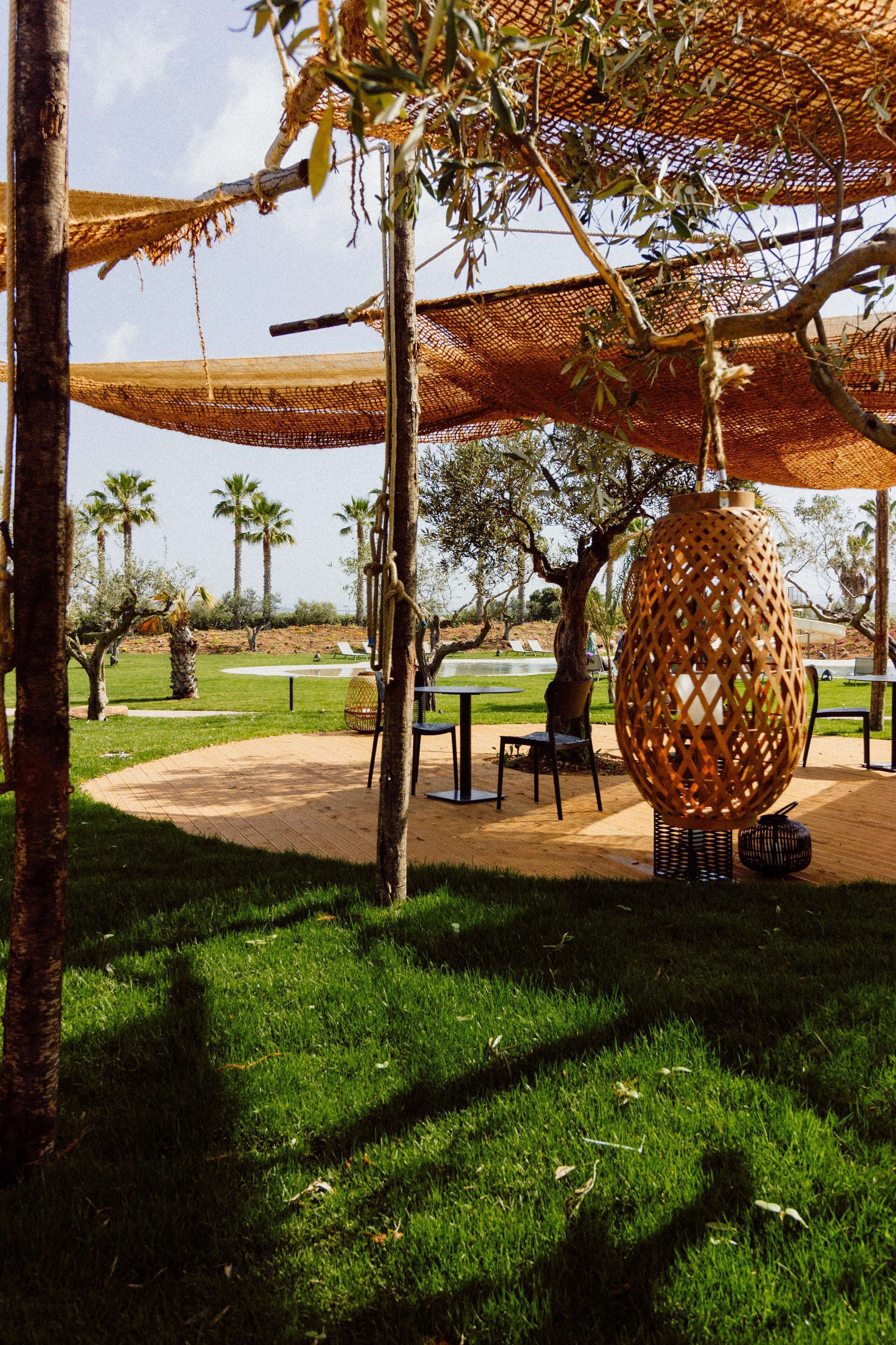 Un parco con posti a sedere all'aperto, una grande lampada intrecciata e palme.