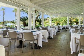 A covered outdoor dining area with tables set for guests, surrounded by palm trees and a view of the landscape. - Mangia's Selinunte Resort (Castelvetrano)