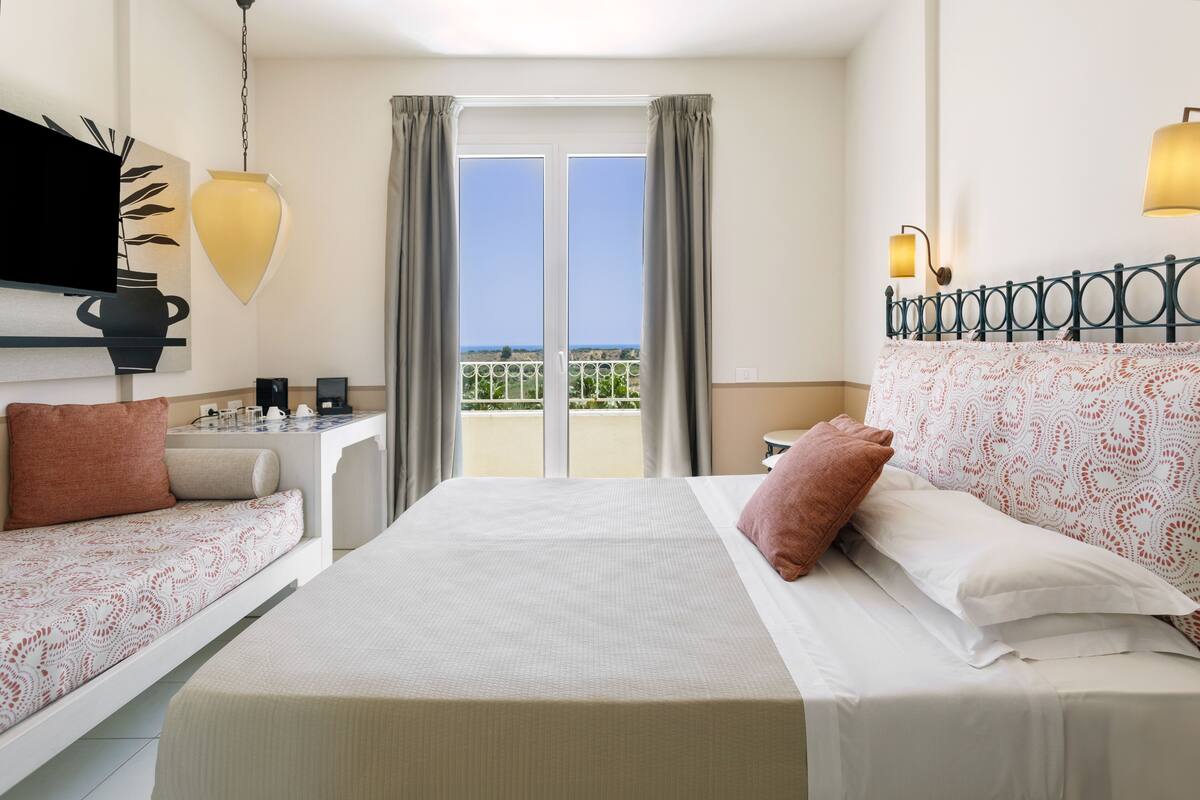 Une chambre d’hôtel avec un grand lit, un canapé, une télévision, un balcon avec vue et une lampe.