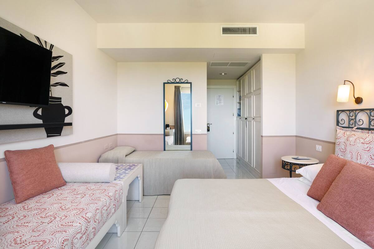 Une chambre d’hôtel avec deux lits, un téléviseur fixé au mur, une petite table et un miroir.