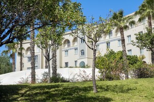 Un hotel de varios pisos con fachada de color claro, ventanas arqueadas y un balcón con detalles azules y blancos.