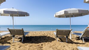 A beach with two white umbrellas and two lounge chairs facing the sea. - Mangia's Selinunte Resort (Castelvetrano)