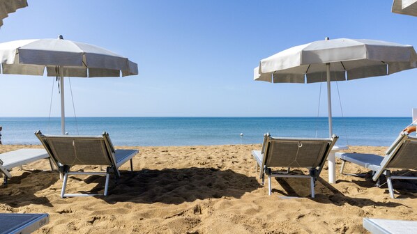 A beach with two white umbrellas and two lounge chairs facing the sea. - Mangia's Selinunte Resort (Castelvetrano)