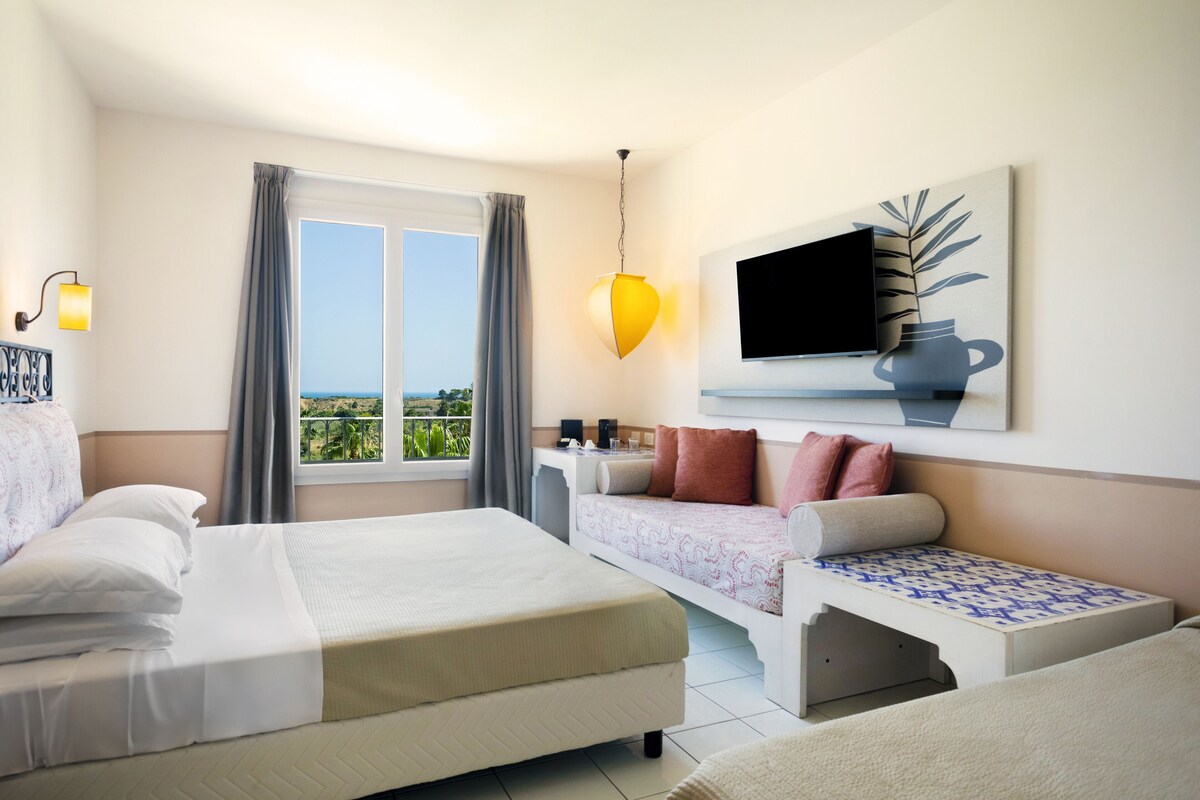 A hotel room with a bed, a sofa, a TV, and a window with curtains.