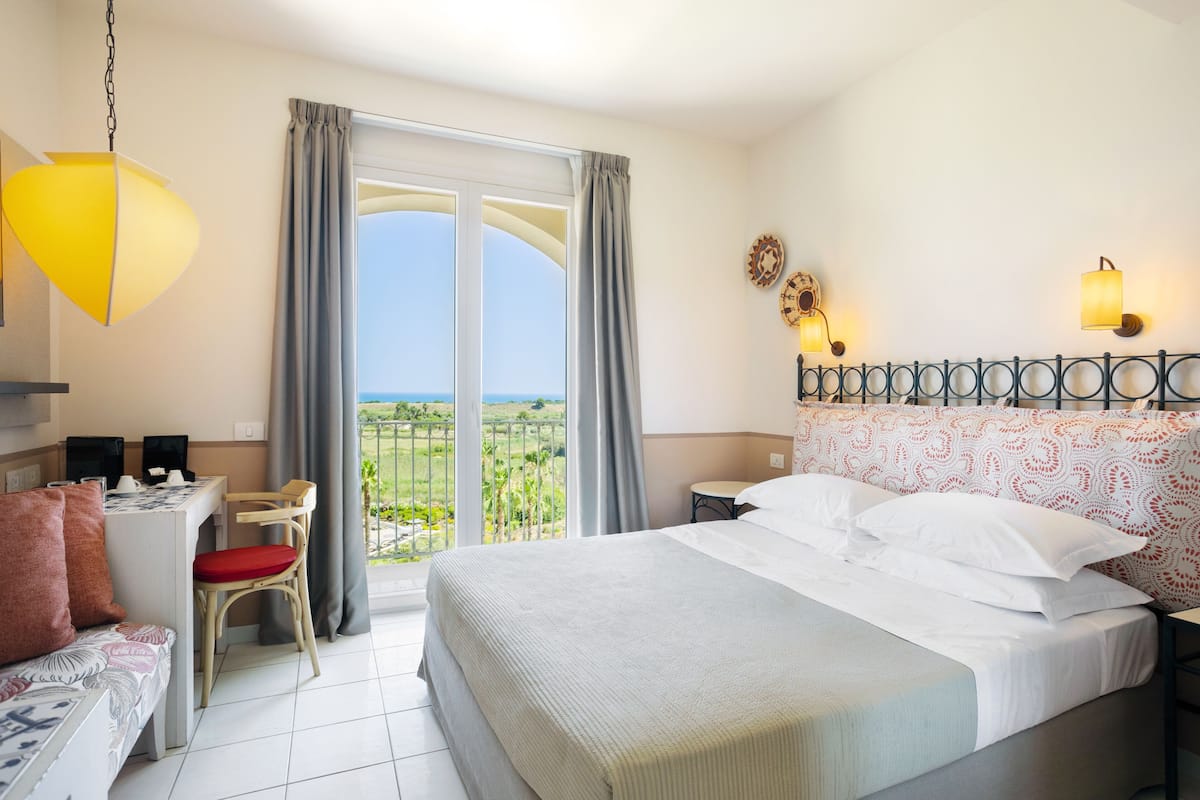 Une chambre d’hôtel comprenant un lit, un bureau, une chaise, un canapé, un balcon avec vue et un luminaire suspendu.