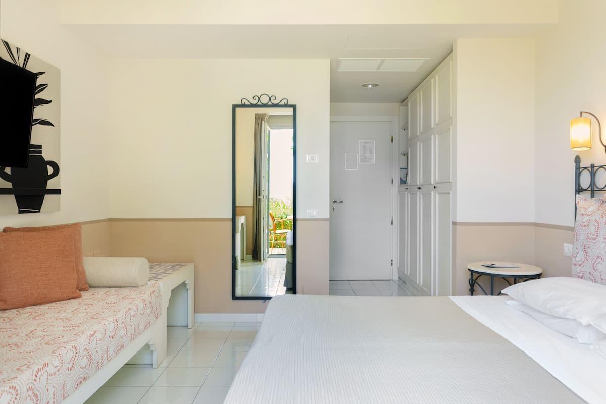 Une chambre d’hôtel comprenant un lit, un canapé, une petite table, un miroir et une porte donnant sur un balcon.