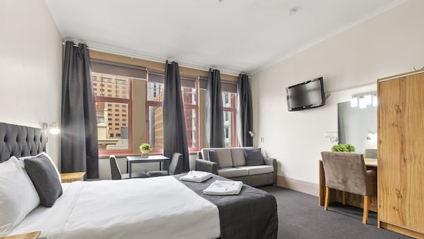 A hotel room with a large bed, a desk, a chair, a sofa, and a TV mounted on the wall.