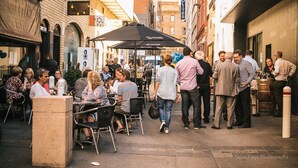 An outdoor café with tables and chairs, surrounded by brick buildings and a street.