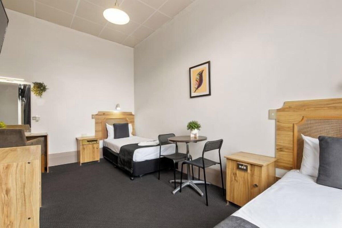 Una camera d'albergo con un letto, una scrivania, una sedia, un tavolino e un comodino.