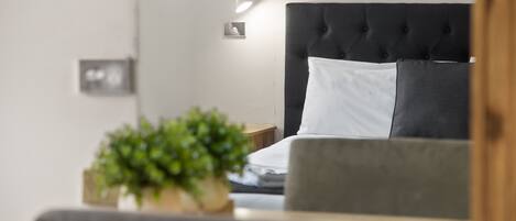 Un dormitorio moderno con cabecera capitonada, una mesita de noche con lámpara y una planta en maceta.