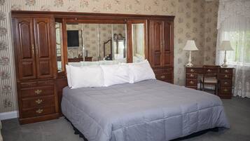 A bedroom with a large bed, wooden wardrobe, and a desk with a chair.