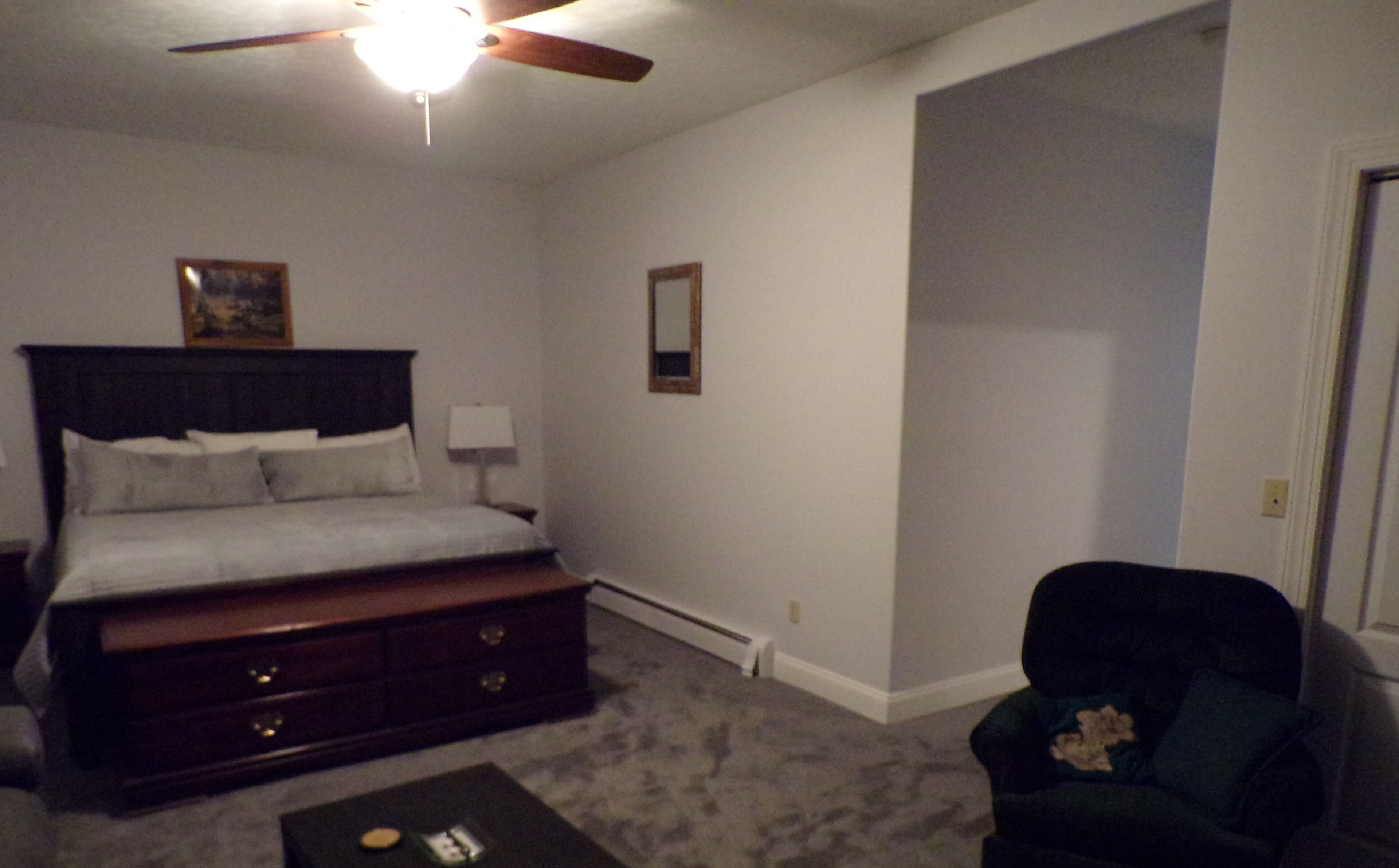 A bedroom with a bed, dresser, chair, and ceiling fan.