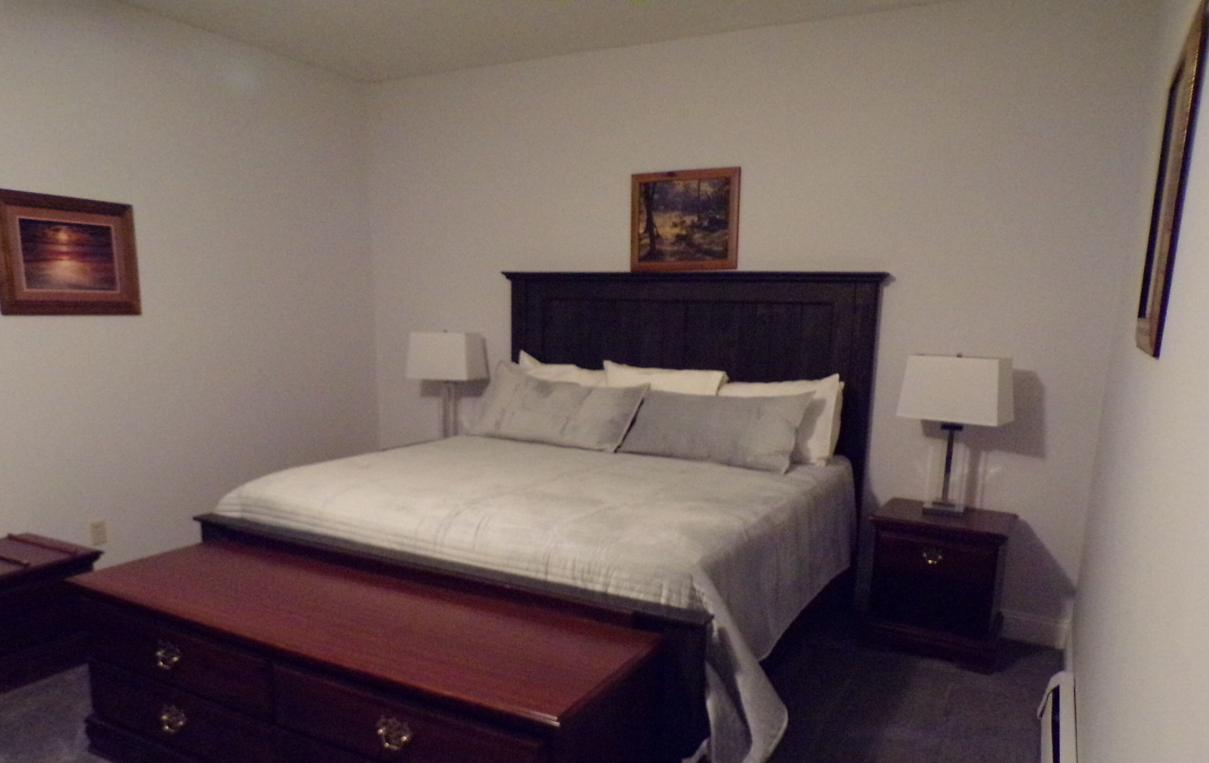 Habitación de hotel ordenada con una cama grande, dos mesitas de noche, un banco de madera y un cuadro en la pared.