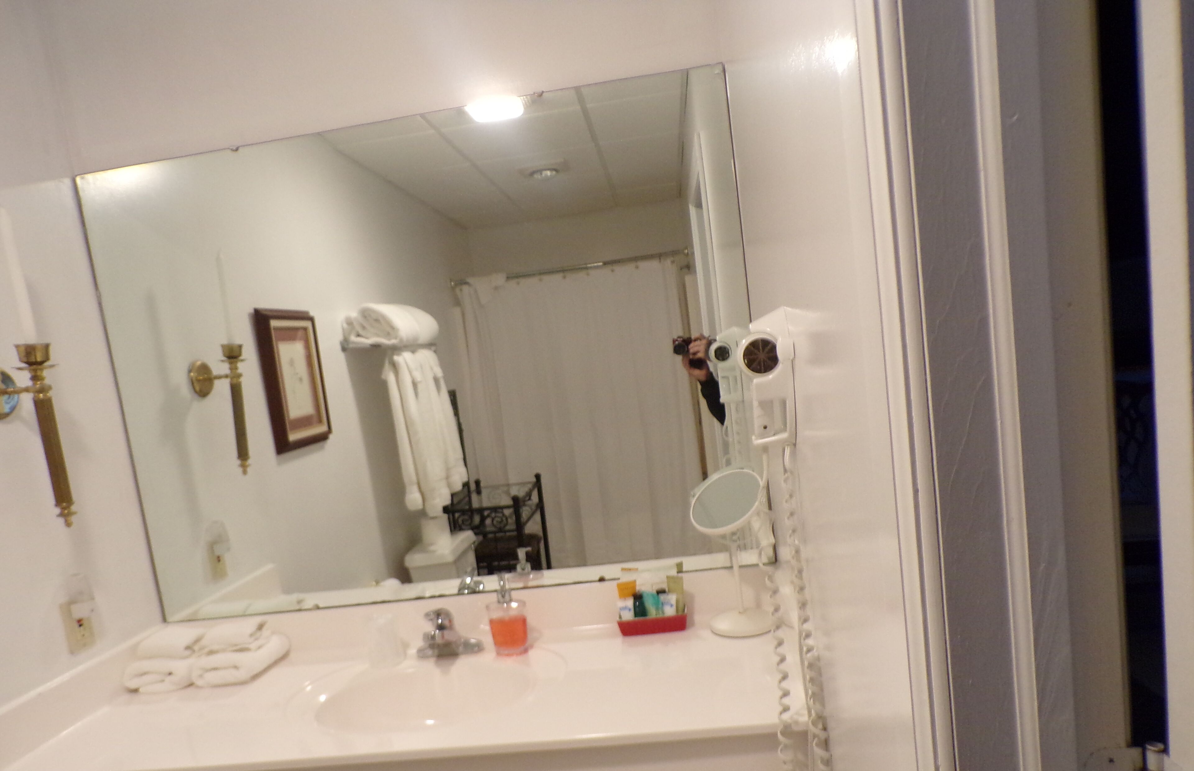 Un baño con un espejo grande, un lavabo con artículos de aseo y una cortina de ducha.