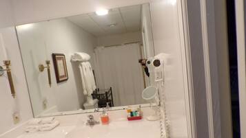 Un baño con un espejo grande, un lavabo con artículos de aseo y una cortina de ducha.