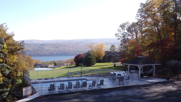 A gazebo with outdoor seating, a fenced tennis court, and a view of a lake and hills. - Long House Manor B And B (Watkins Glen)