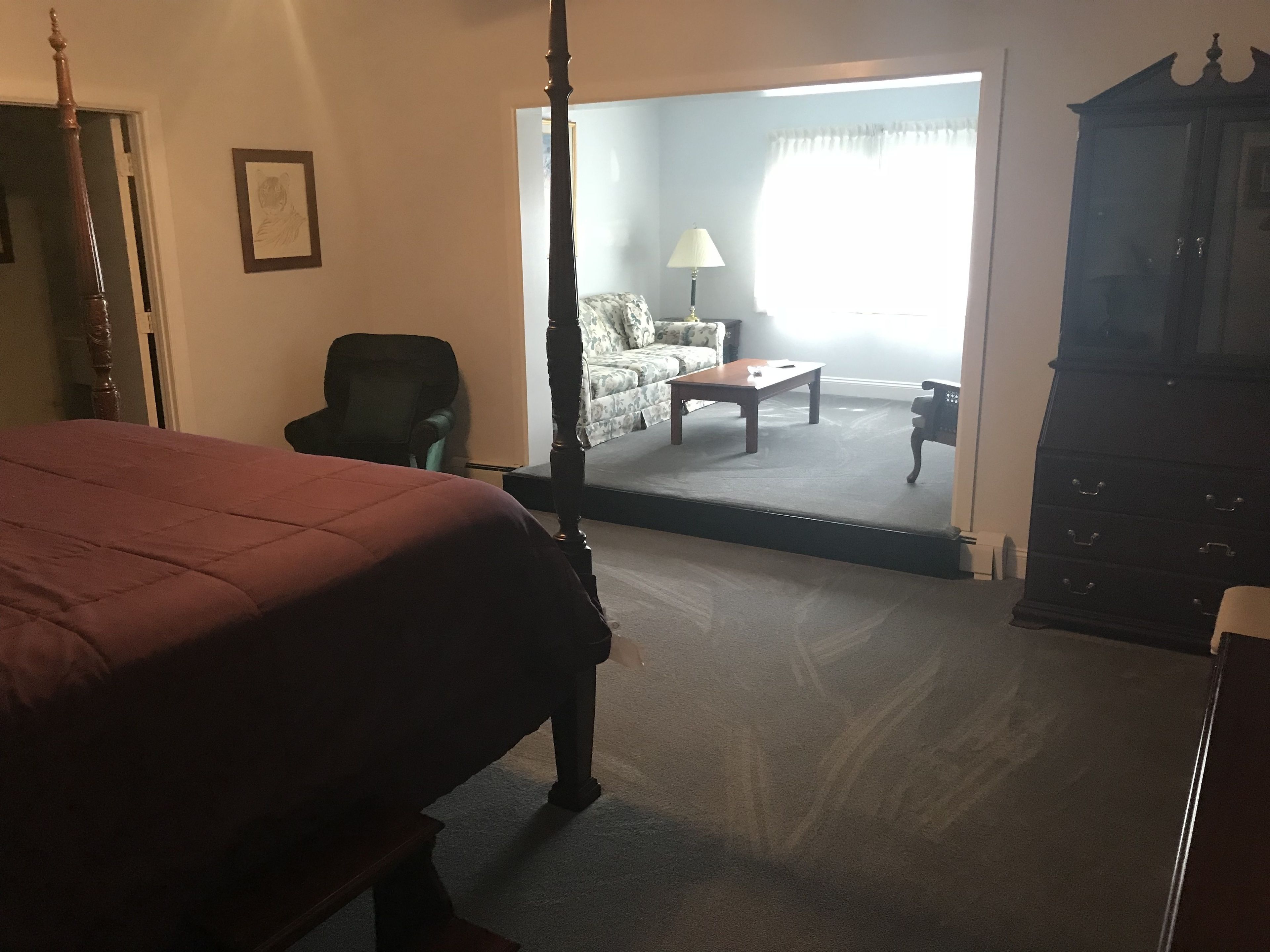 A bedroom with a four-poster bed, a chair, a sofa, a coffee table, and a cabinet.
