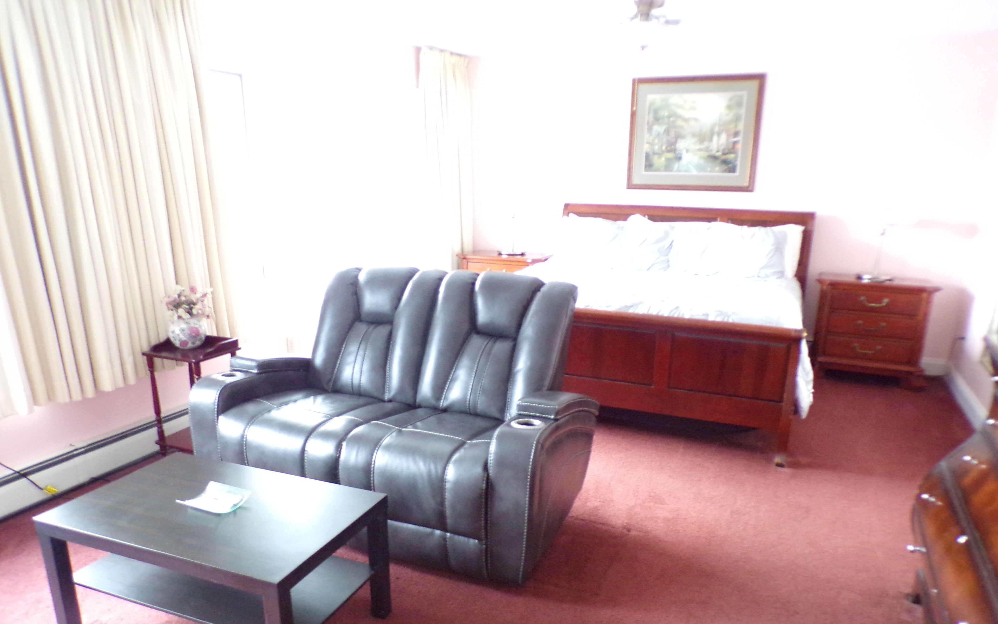A hotel room with a leather armchair, a wooden bed, a nightstand, and a desk with a lamp.