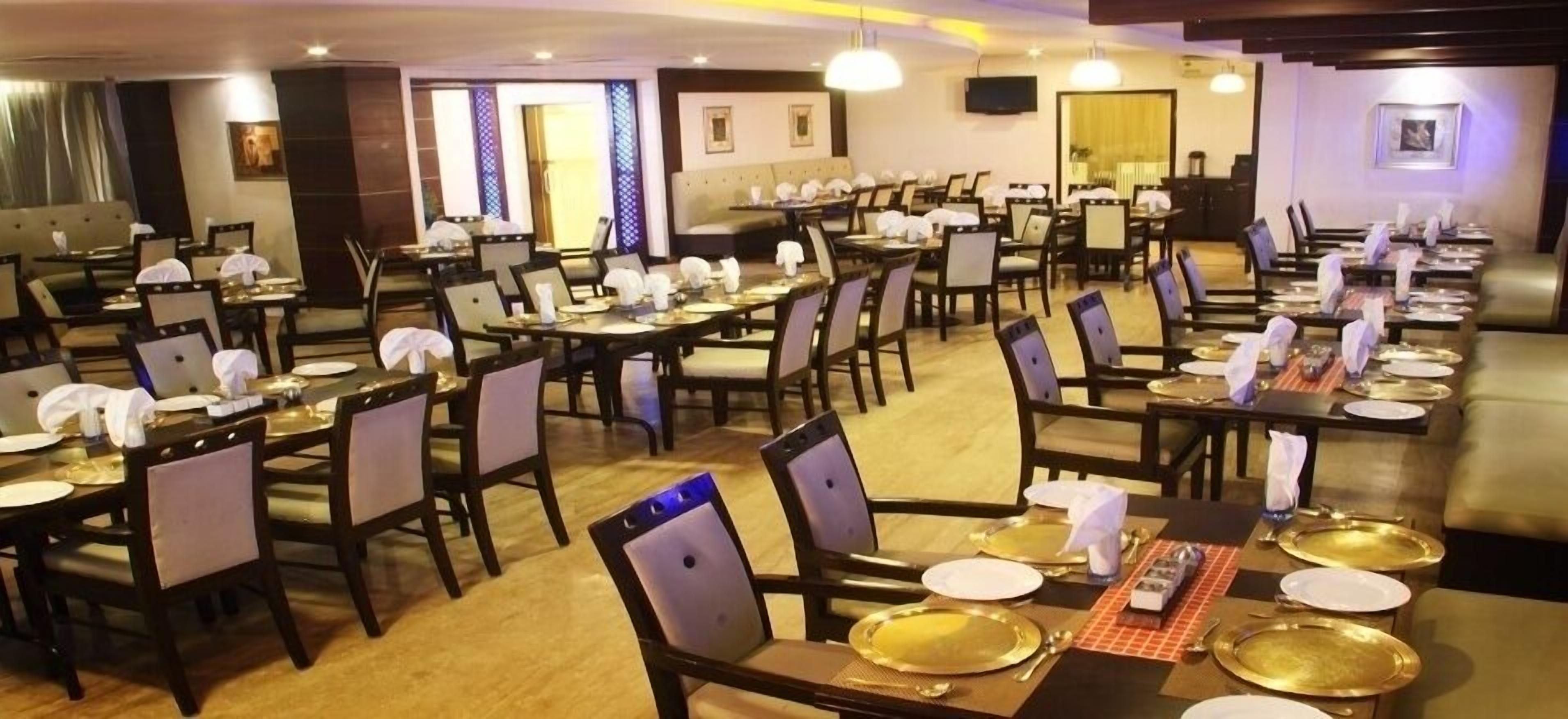 A restaurant with multiple dining tables set with white napkins, gold-colored plates, and cutlery.