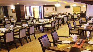 A restaurant with multiple dining tables set with white napkins, gold-colored plates, and cutlery. - The Chevron Hotel (Bengaluru)