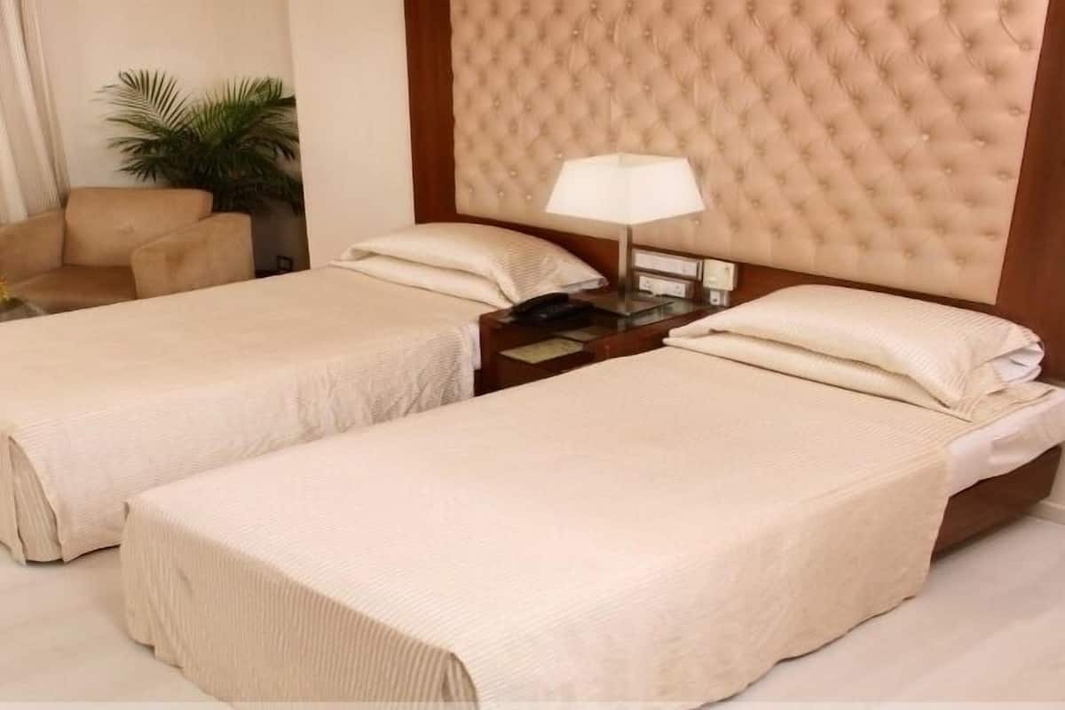 Una habitación de hotel con dos camas individuales, una mesita de noche con lámpara, una silla y una planta en maceta.