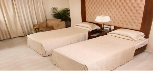 Two single beds with matching headboards, a small table, and a chair near the window.