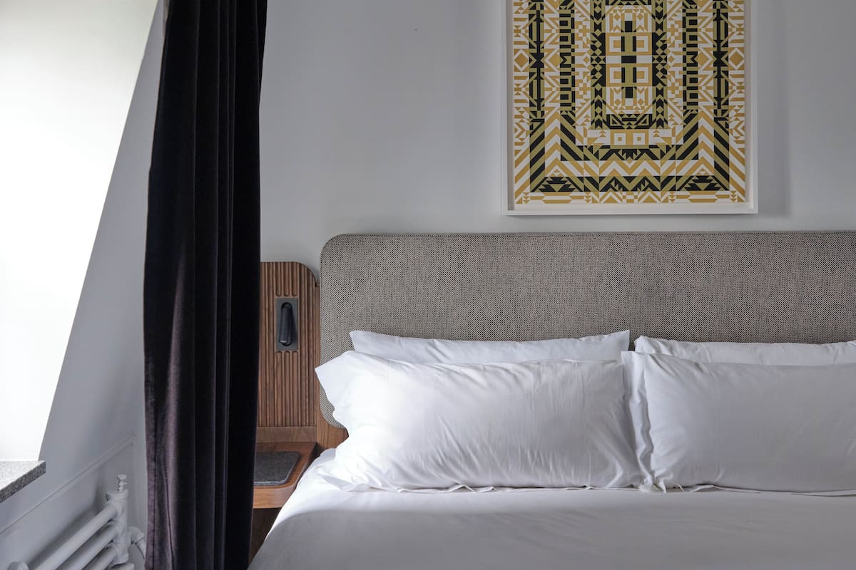 A neatly made bed with white linens, a patterned headboard, and a geometric wall art piece.