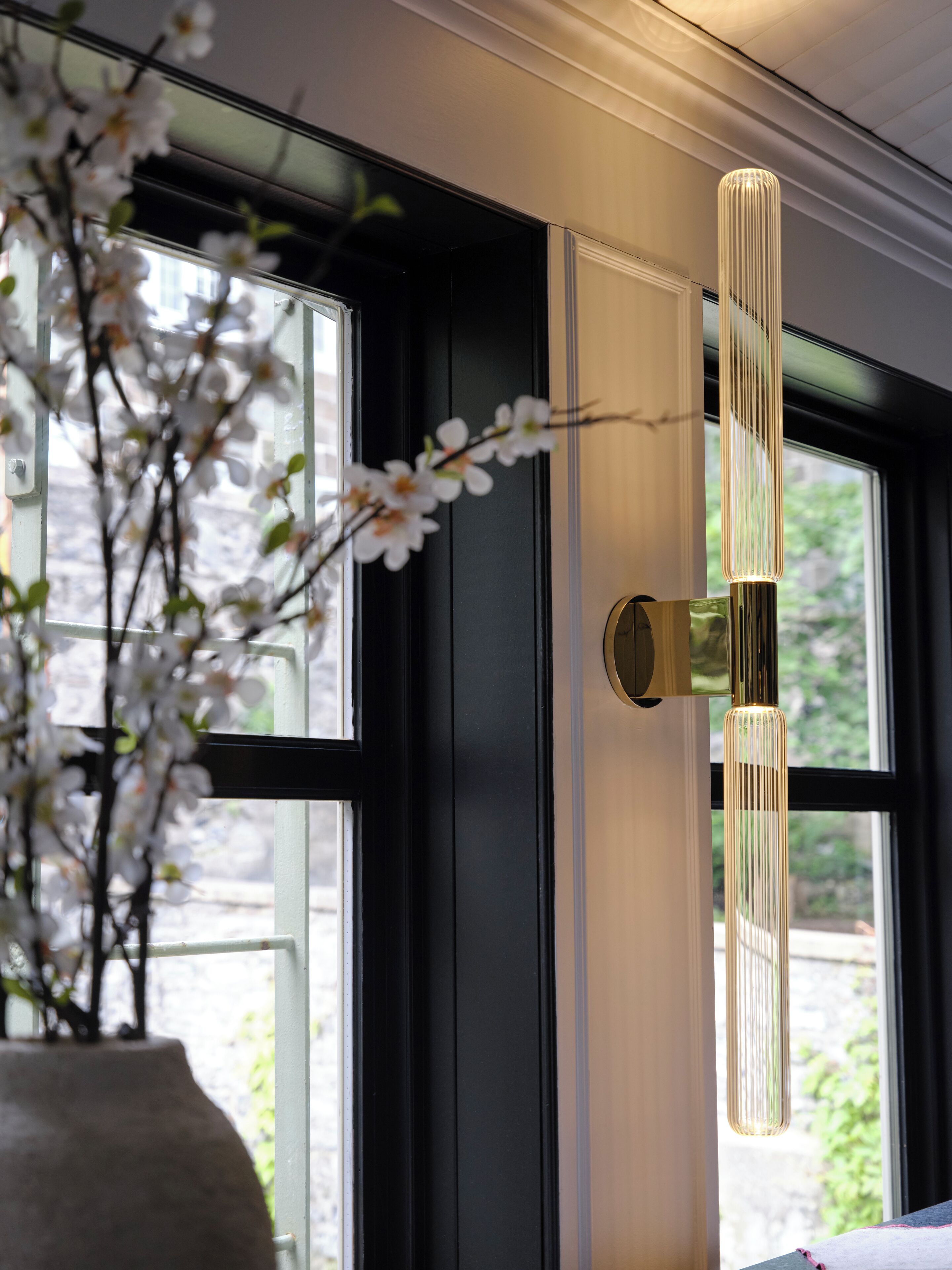 A modern door with a vertical light fixture and a vase with white flowers.