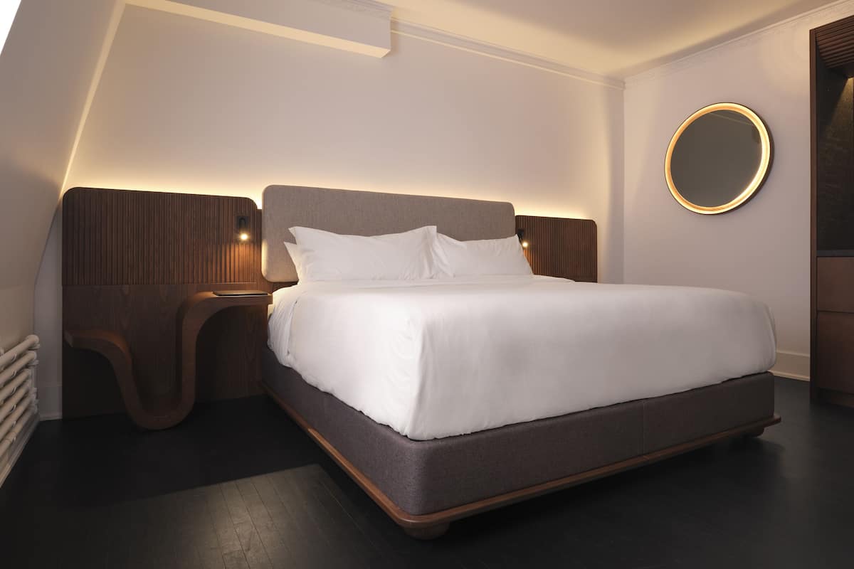 A modern bedroom with a large bed, wooden headboard, bedside tables, and a round mirror on the wall.