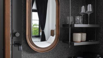 Un baño moderno con un lavabo negro, un espejo y una repisa con vasos y tazas.