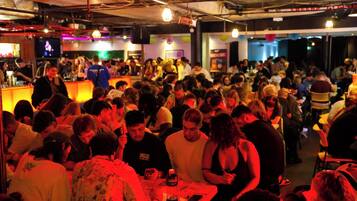 Un bar o discoteca concurrido, con gente sentada y de pie alrededor de las mesas.