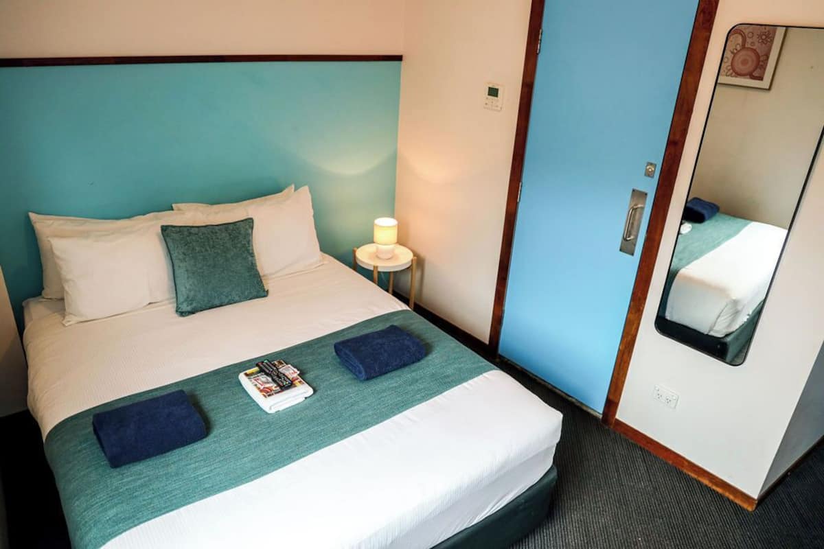 A neatly made bed with pillows, a bedside lamp, and a magazine on the bed.