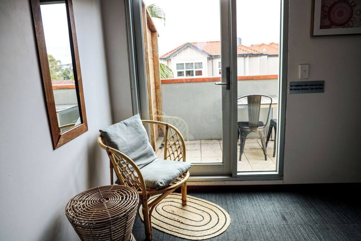 A room with a wicker chair, a small round table, and a sliding glass door leading to an outdoor area with chairs.