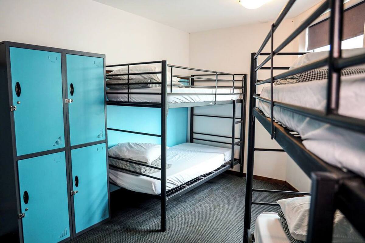 A bunk room with three bunk beds, a set of blue lockers, and a carpeted floor.