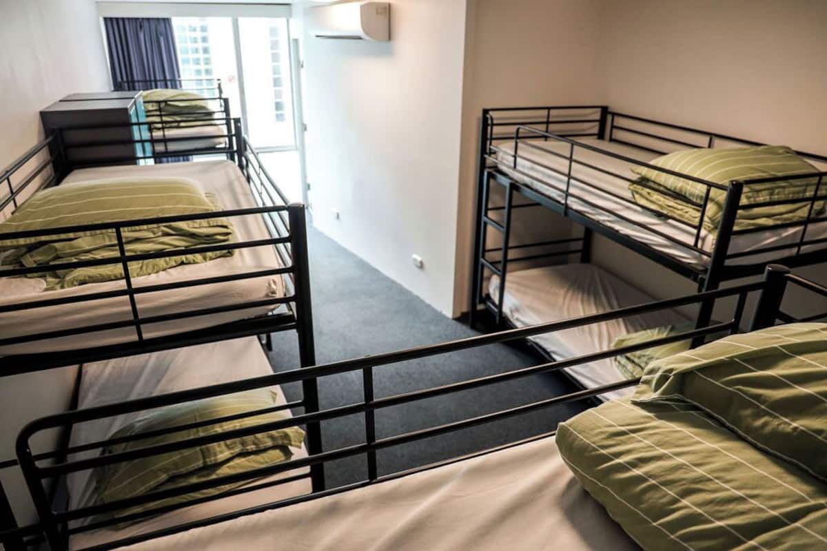 A dormitory room with bunk beds, a window with curtains, and a wall-mounted air conditioning unit.