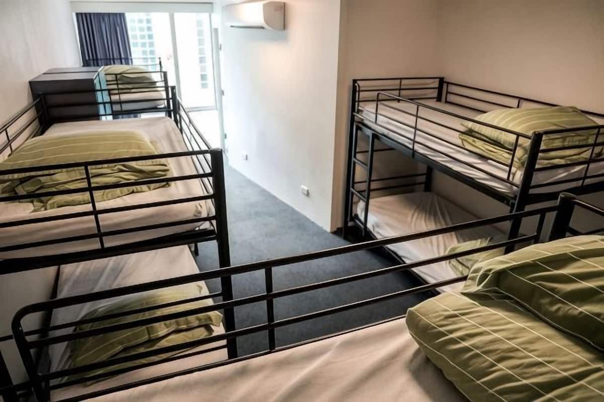 A dormitory room with bunk beds, a window with curtains, and a small desk with a chair.