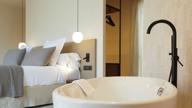 A modern bedroom with a large bathtub, a bed with white linens, and a wall-mounted control panel. -  1881 Hotel Balneario Vichy Catalan (Caldes de Malavella)