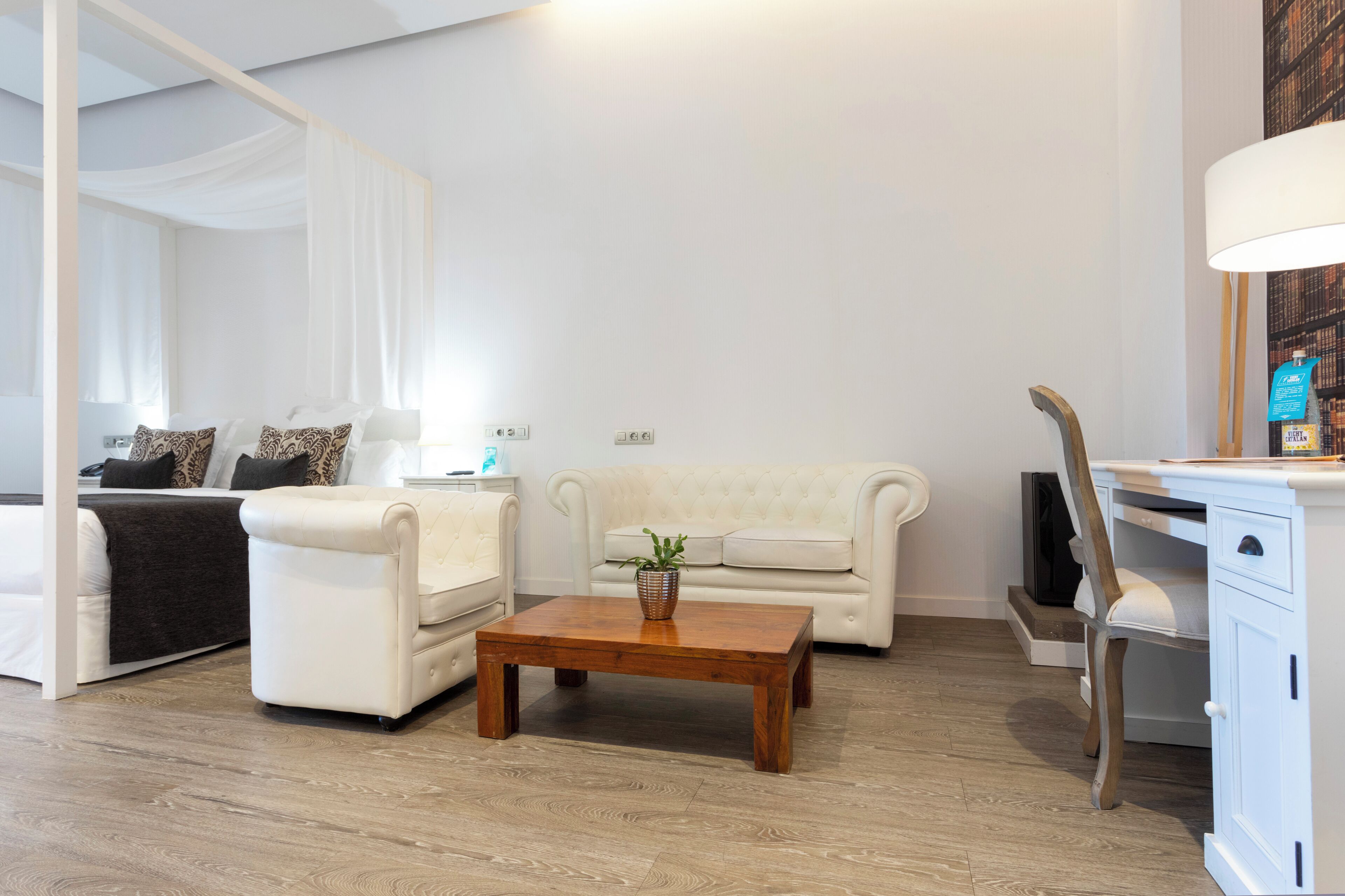 Ein modernes Wohnzimmer mit Bett, einem weißen Sofa, einem Holztisch und einem weißen Schreibtisch mit Lampe.