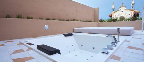 A spa area with a large bathtub, a bench, and a wall-mounted control panel.